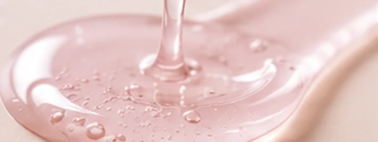 Pale blush translucent serum pool with delicate clear droplets.