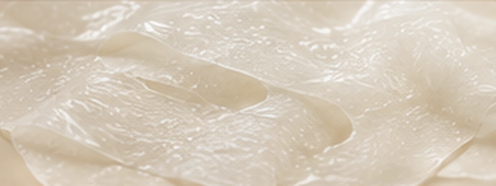Pearl-clear translucent skincare film with soft luminous folds.