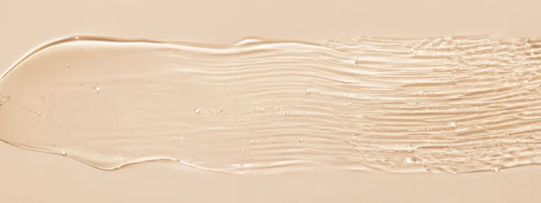 Clear skincare gel with fine soft ripples increasing in density across a warm ivory background.