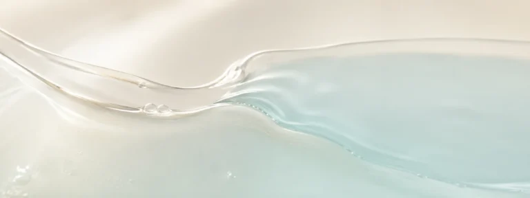 Pearl-clear serum flowing into a cool translucent aqua layer on a warm ivory background.