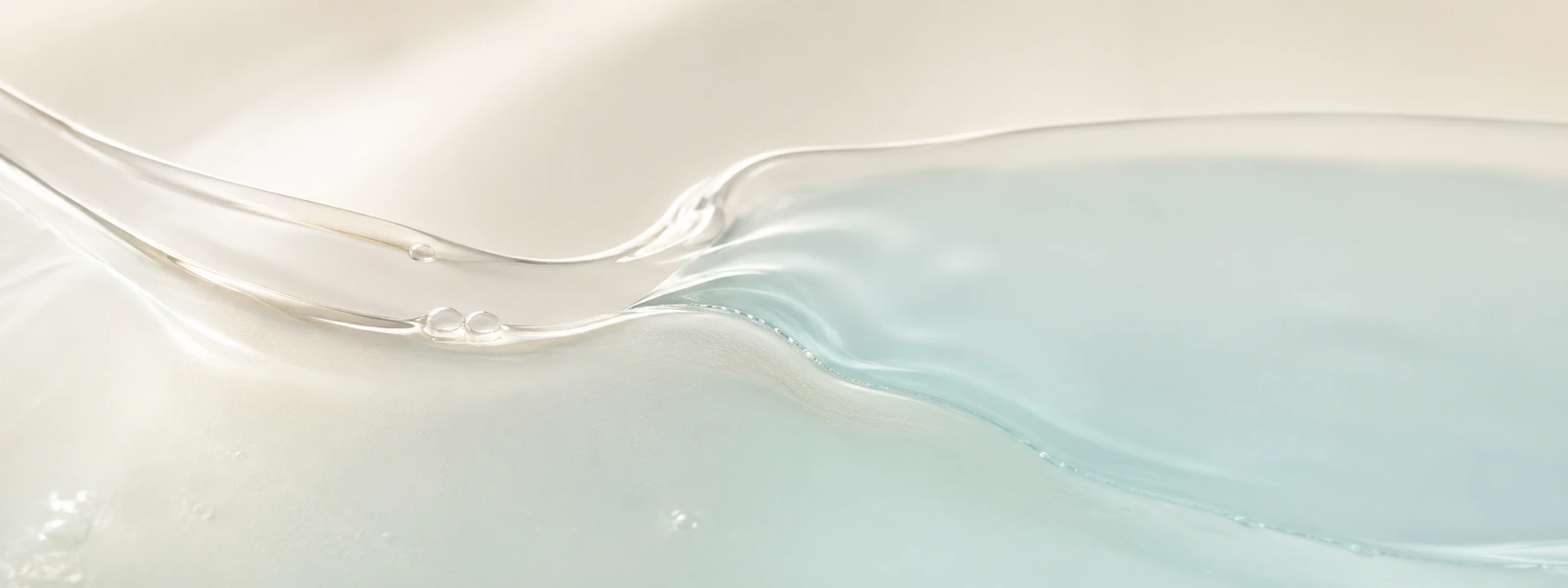 Pearl-clear serum flowing into a cool translucent aqua layer on a warm ivory background.