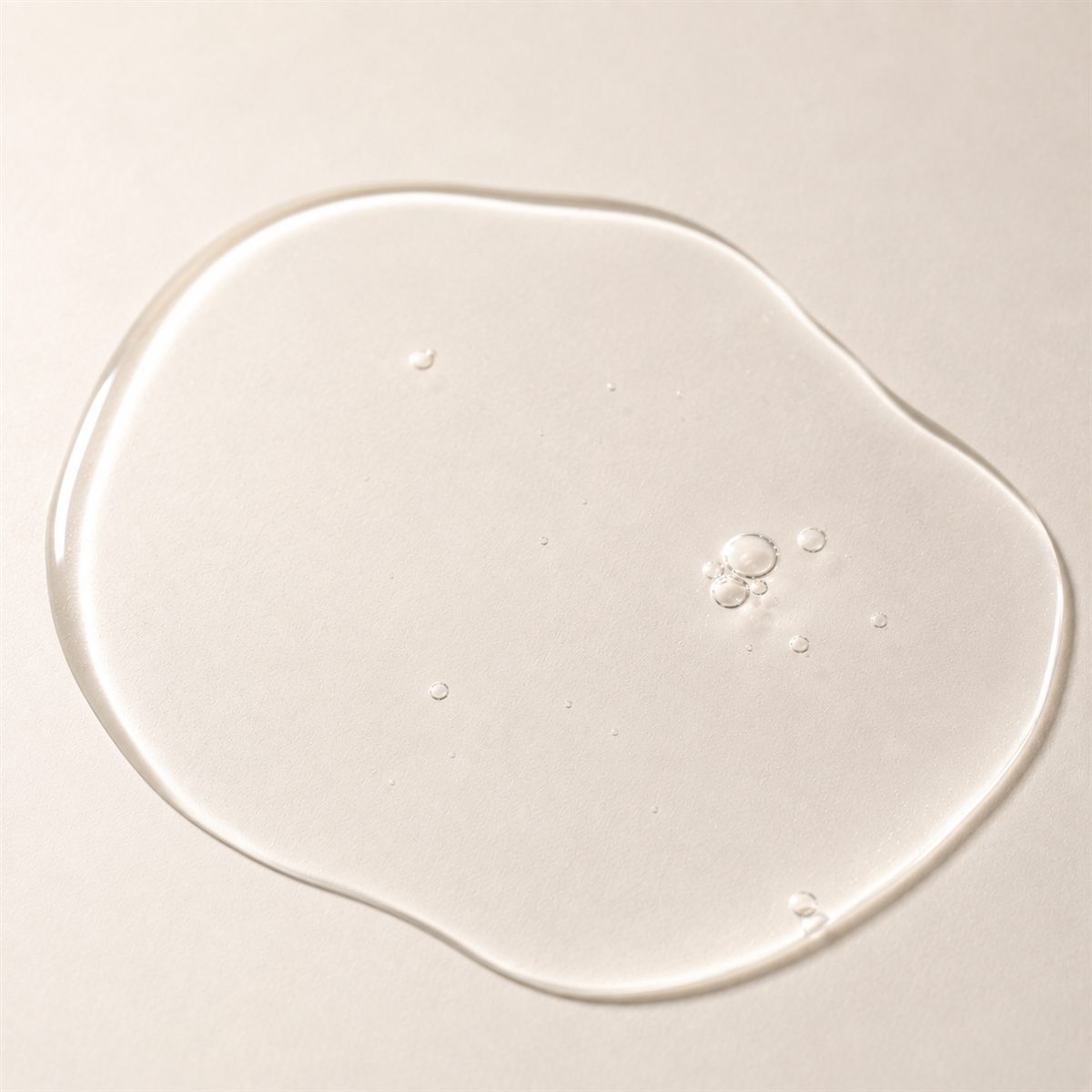 Close-up of a clear watery toner droplet on an ivory background.