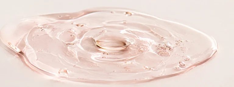 Pearl-clear serum with a faint blush tint, pooled in a soft macro composition.