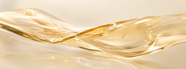 Luminous pearl-gold translucent serum forming a soft flowing wave.
