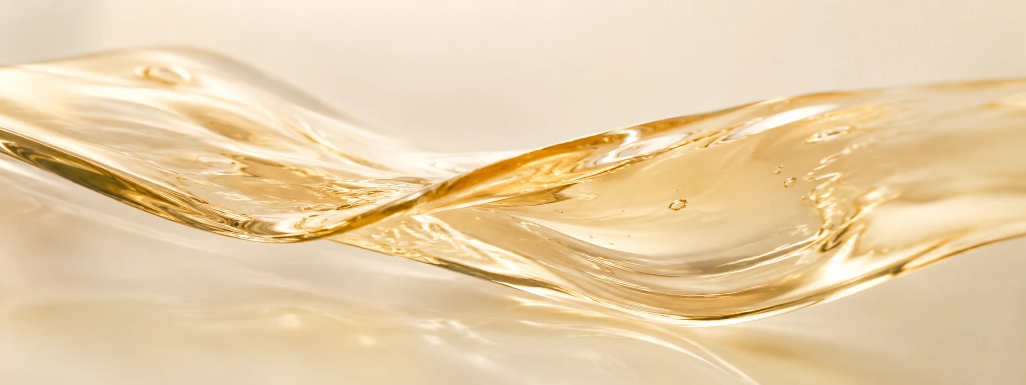 Luminous pearl-gold translucent serum forming a soft flowing wave.