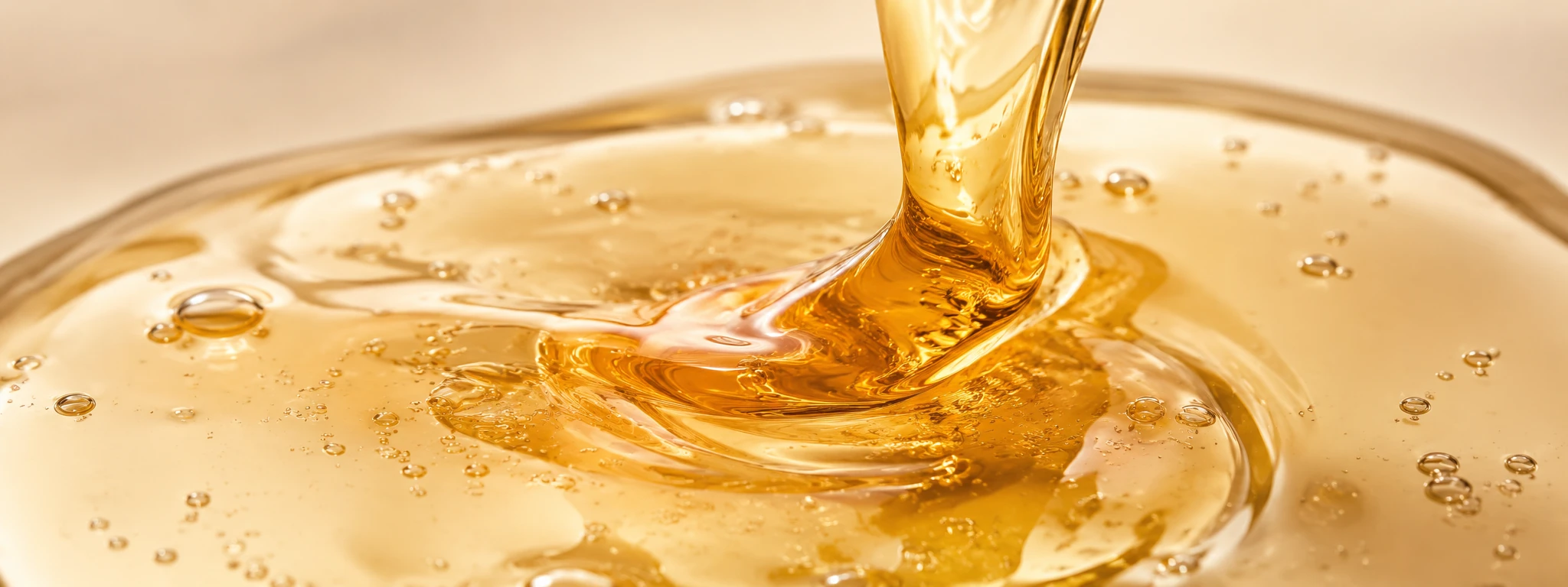 Amber-gold viscous serum pouring into a pool with honey-like translucent folds.